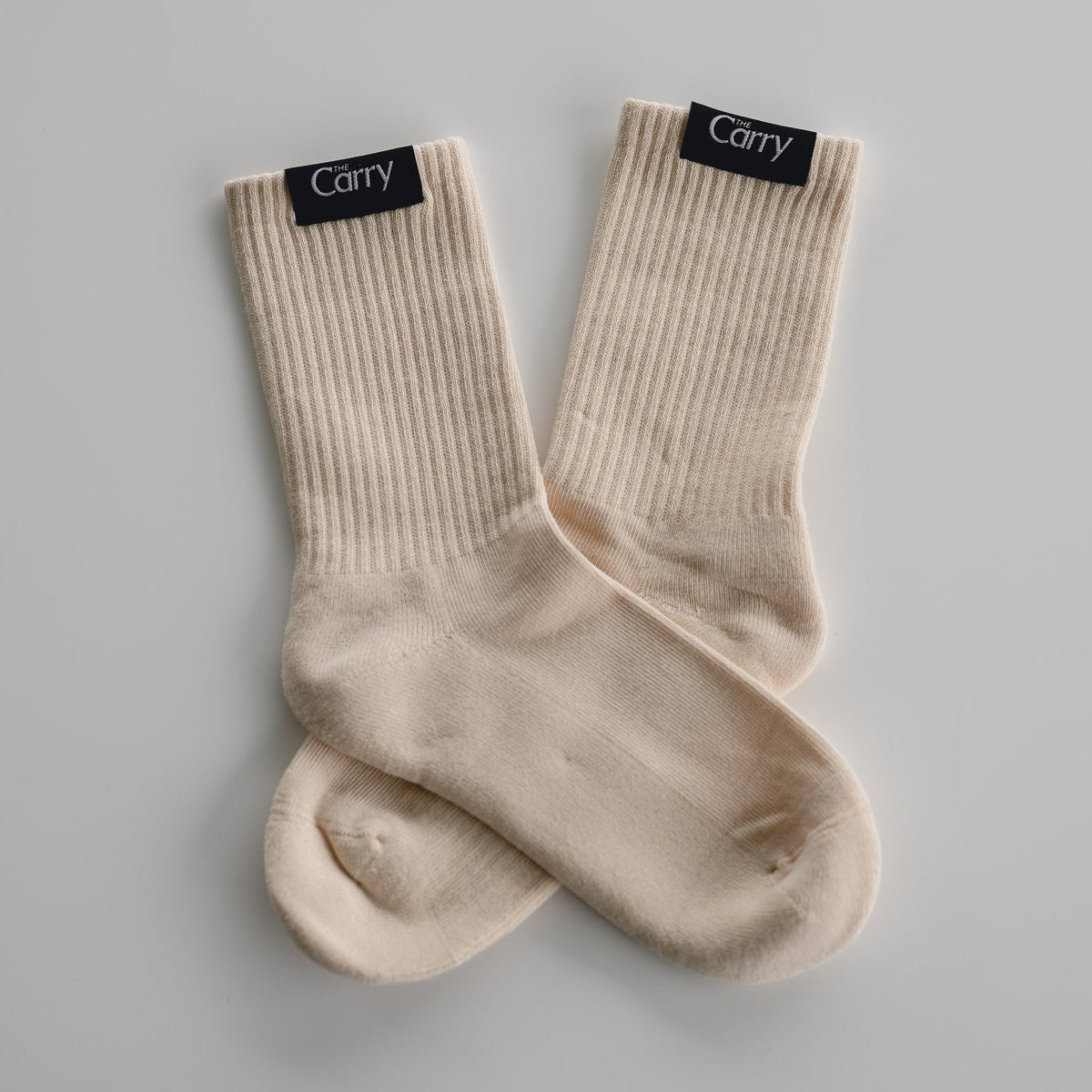 Pair of beige socks with 'Carry' label on a gray background