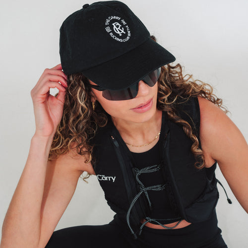 Woman wearing a black branded hat in The Carry Vest and sunglasses with a plain background