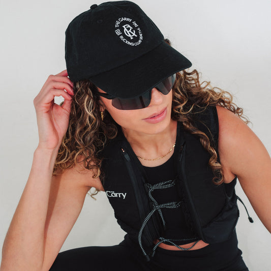Woman wearing a black branded hat in The Carry Vest and sunglasses with a plain background