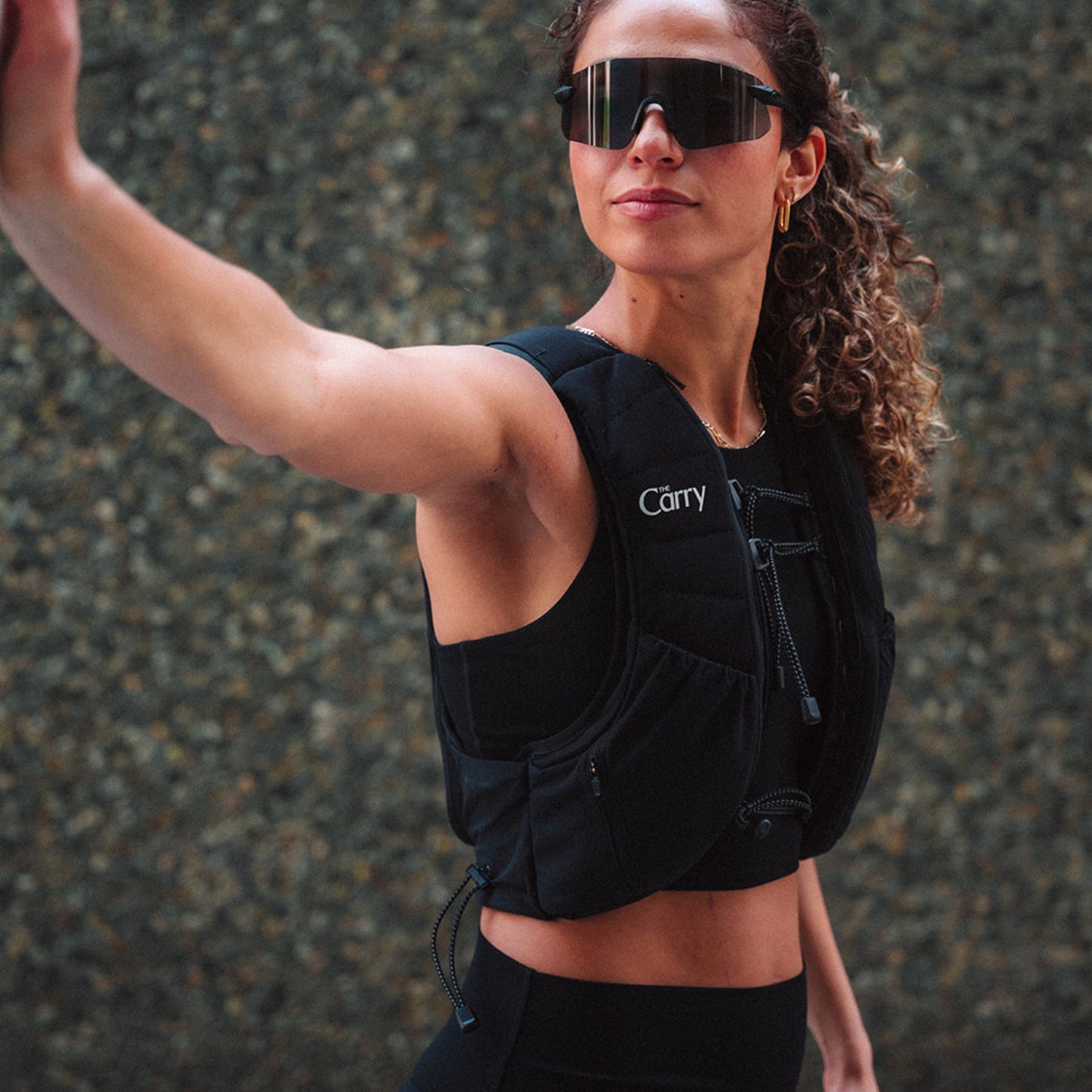 Woman wearing The Carry weighted vest in black against a city stone wall background