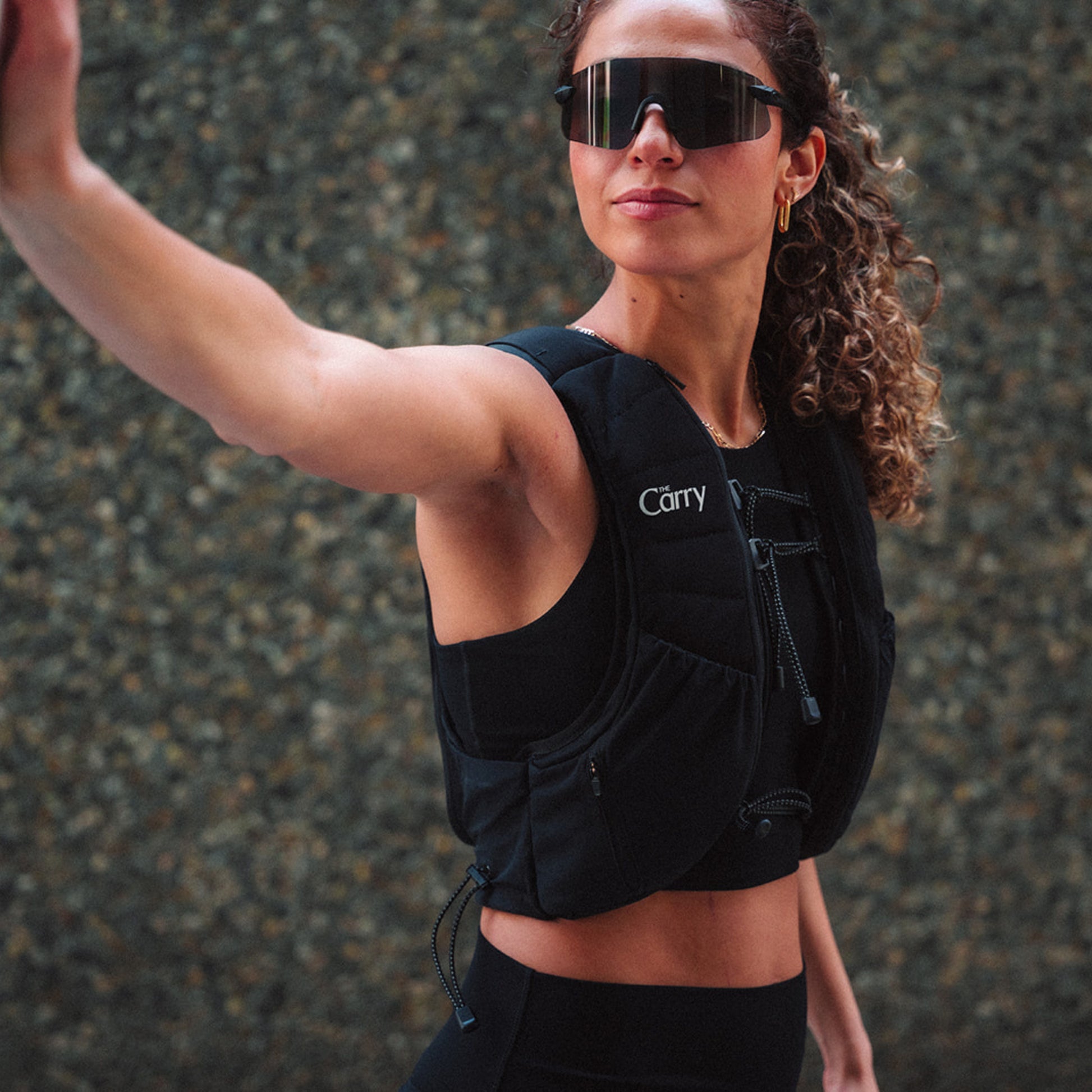 Woman wearing The Carry weighted vest in black against a city stone wall background
