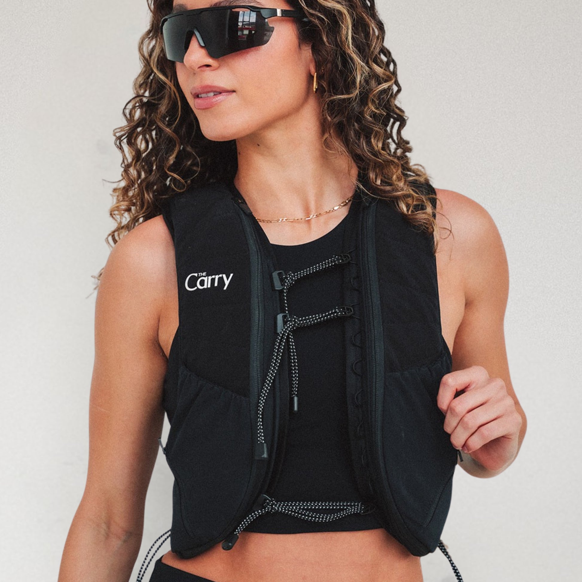 Woman wearing The Carry weighted vest in black against a plain background in sunglasses