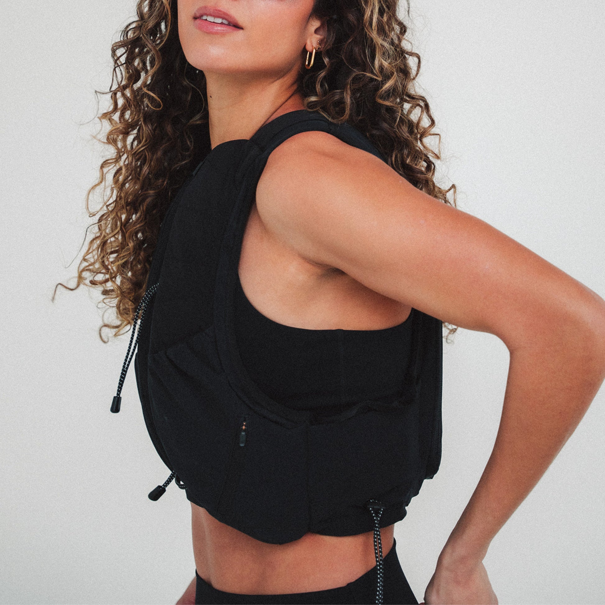 Woman wearing The Carry weighted vest in black against a plain background, side view