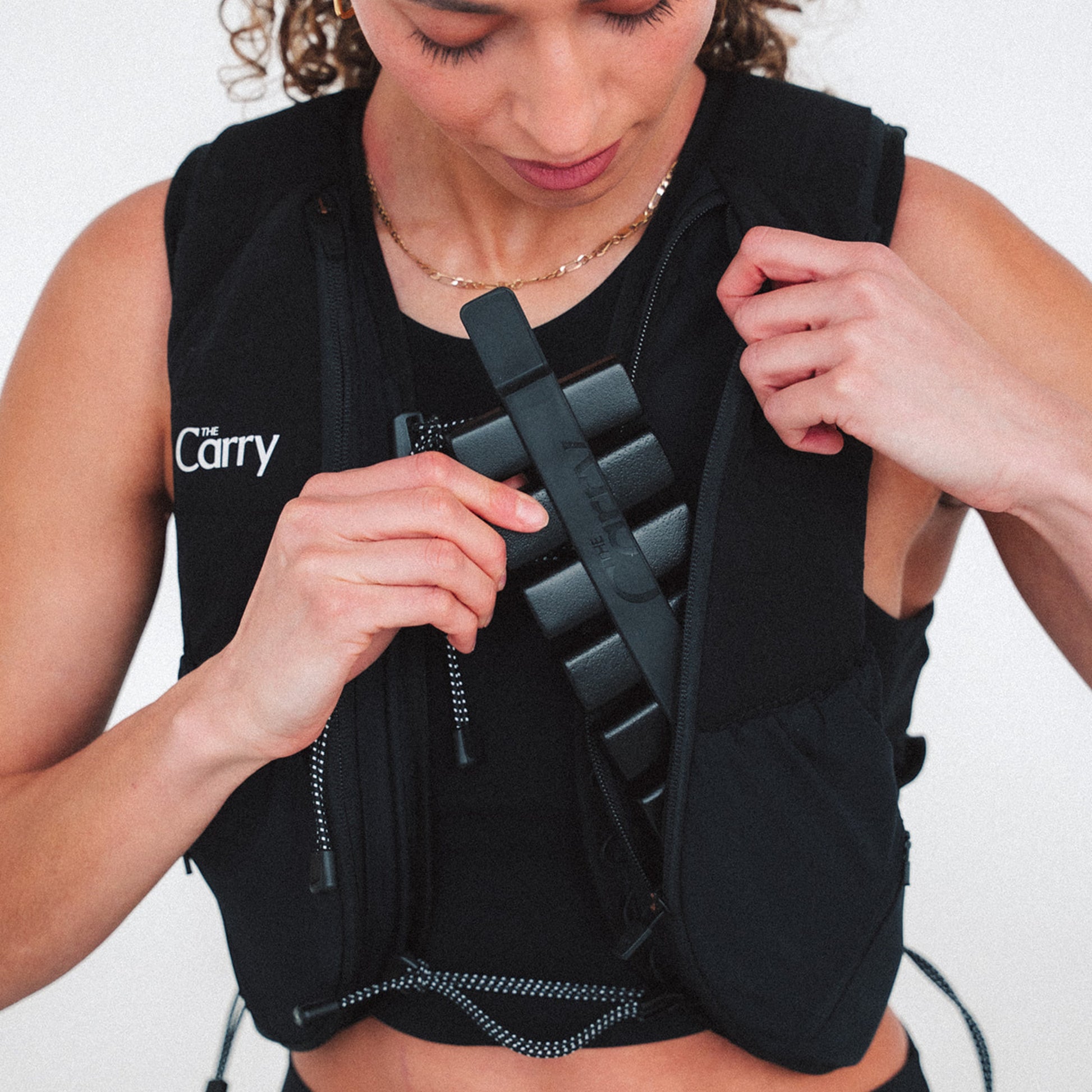 Woman wearing The Carry weighted vest in black against a plain background, pulling out the adjustable weight system