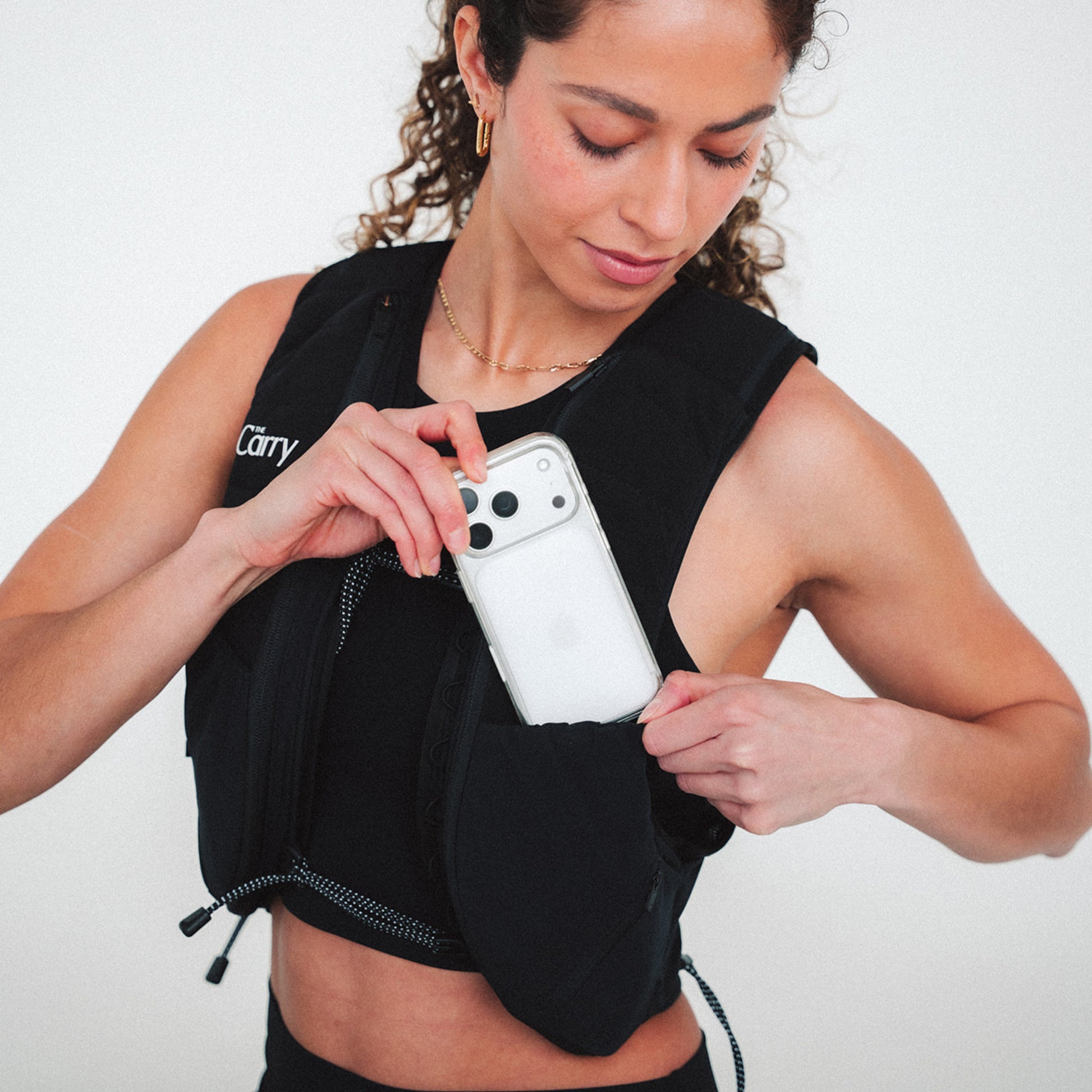 Woman wearing The Carry weighted vest in black against a plain background, pulling out a phone from shell pocket