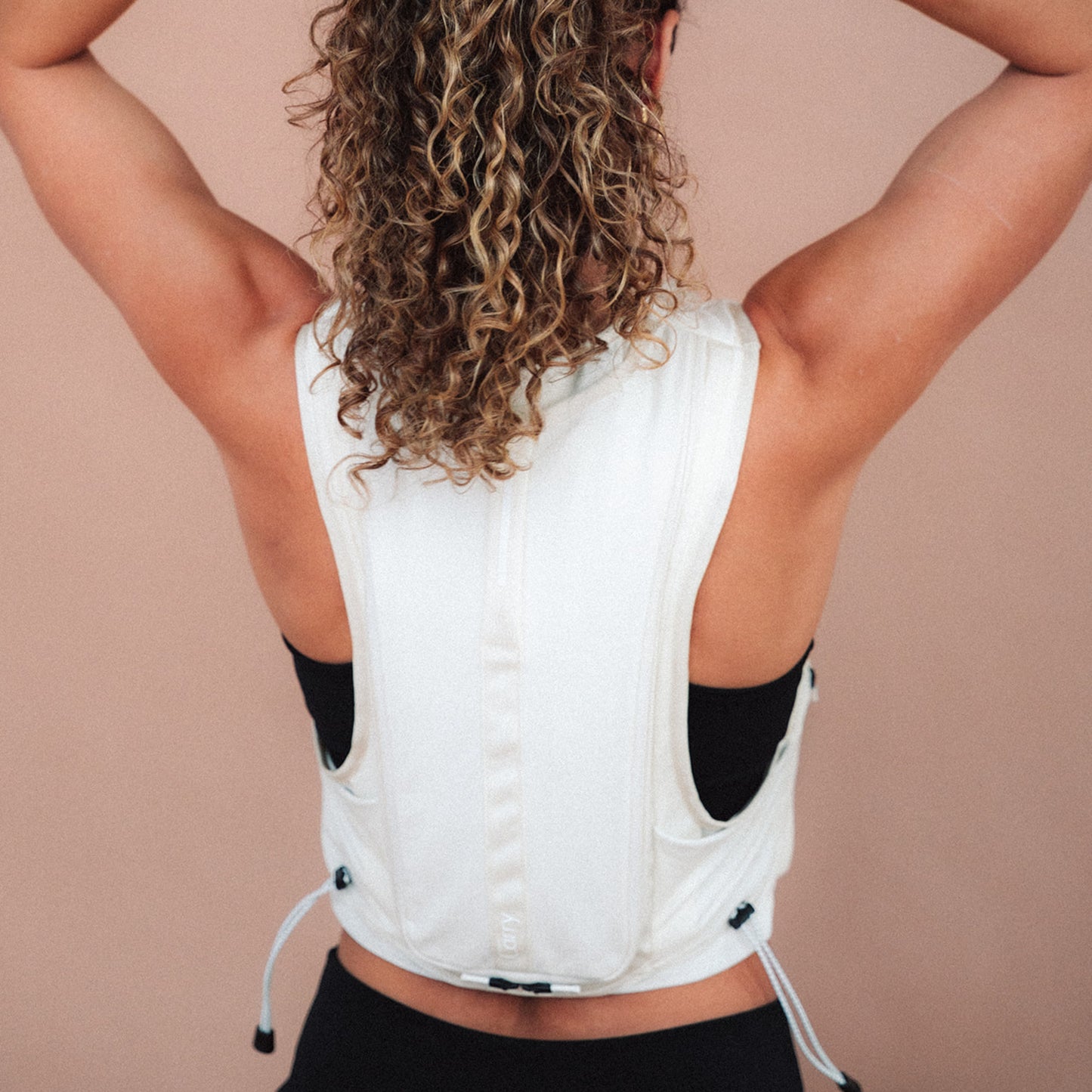 Woman wearing The Carry weighted vest in cream against a plain background, back view