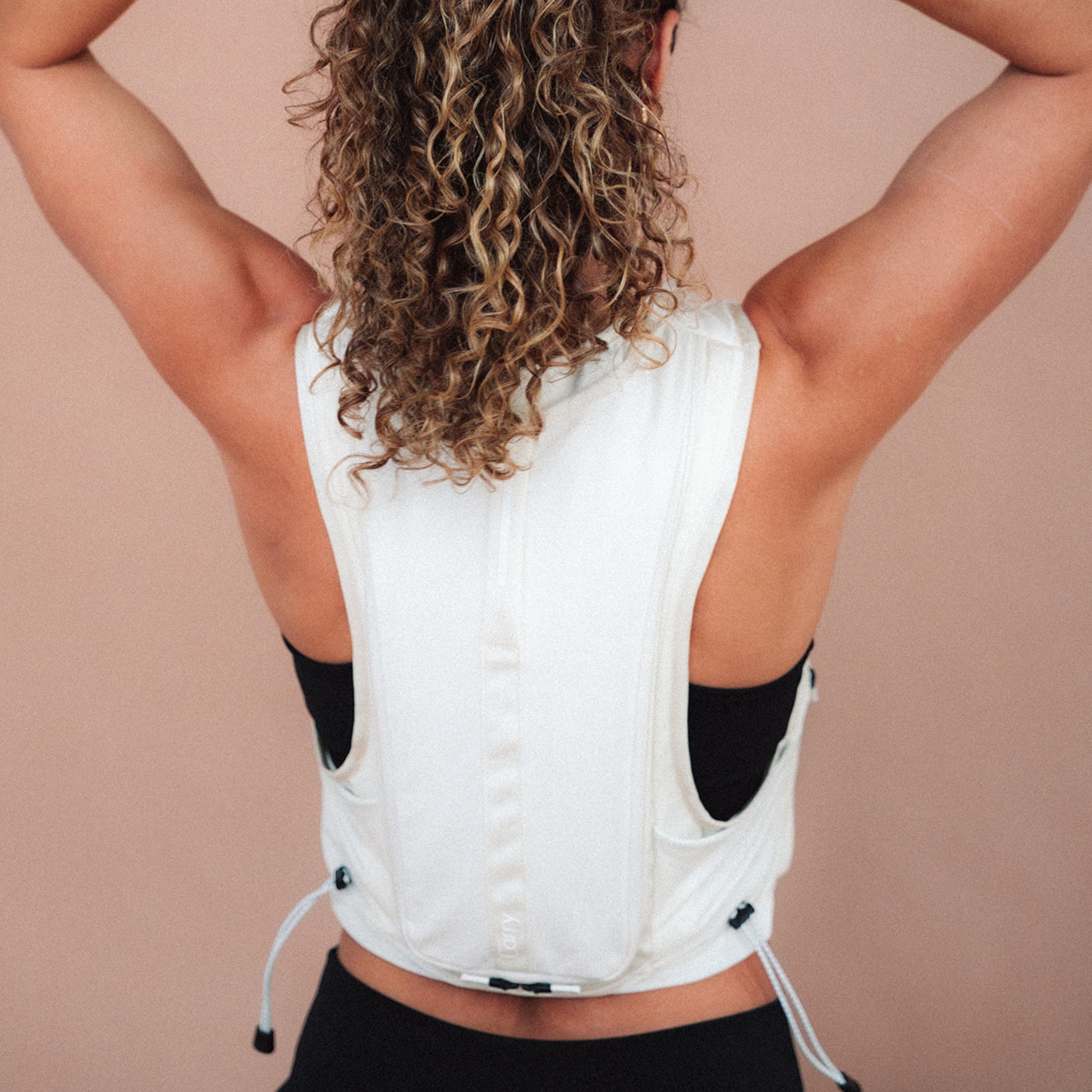 Woman wearing The Carry weighted vest in cream against a plain background, back view