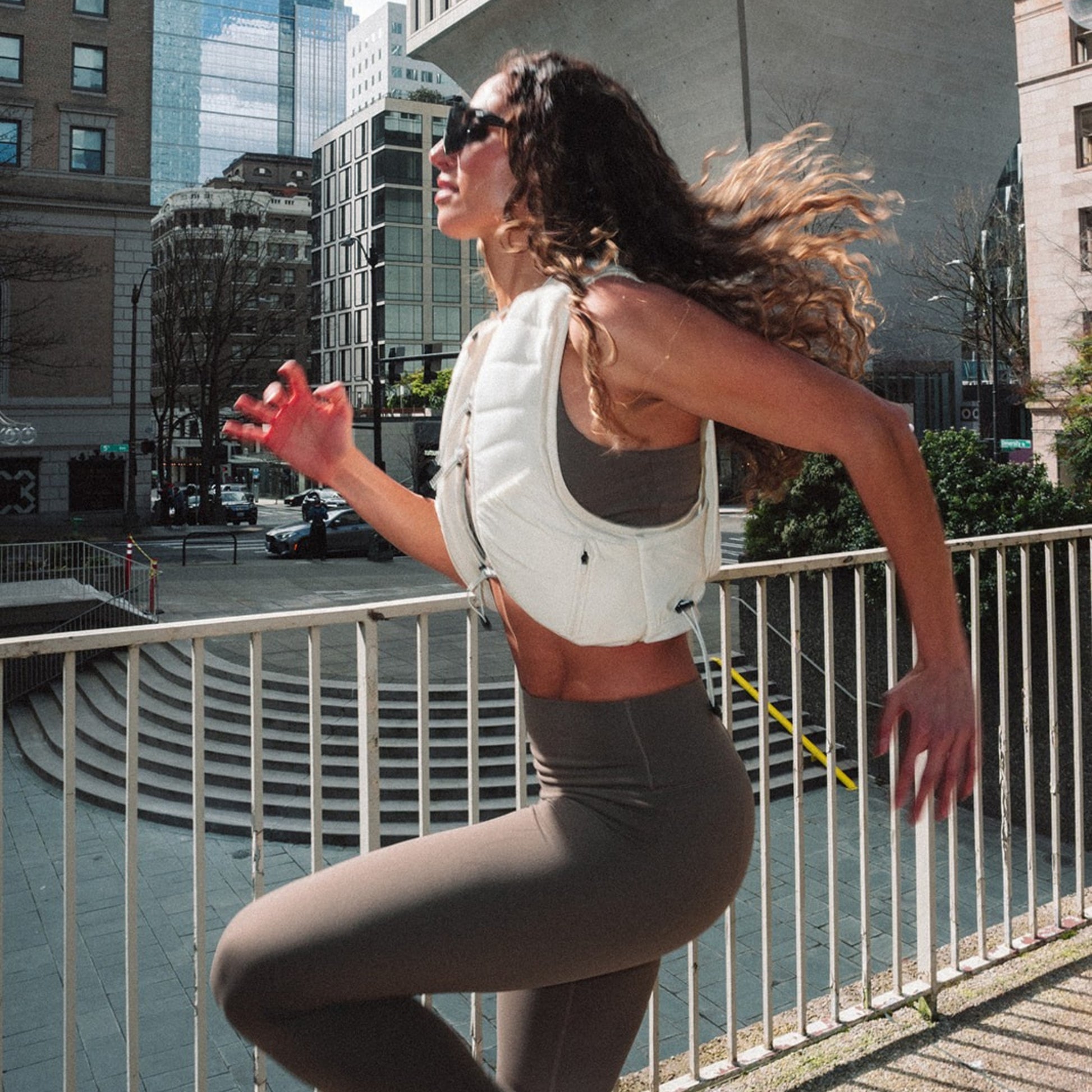 Woman wearing The Carry weighted vest in cream against a city backdrop doing high knee jumps