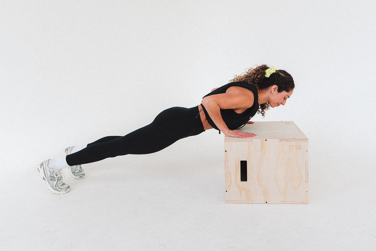 Woman performing push-ups on a wooden box against a white background